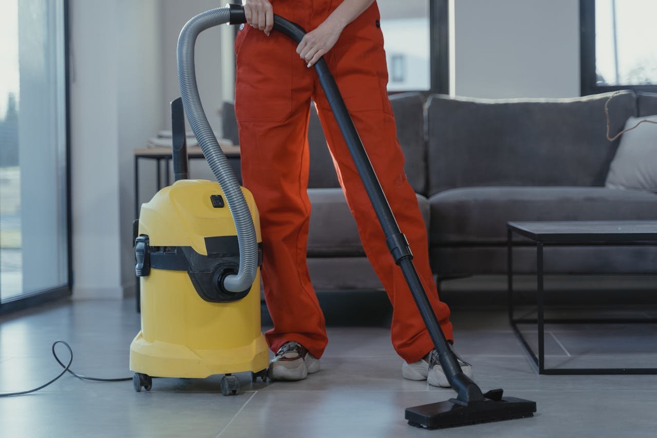 services-02 A professional cleaner in red coveralls vacuums a contemporary living room with a yellow vacuum cleaner.